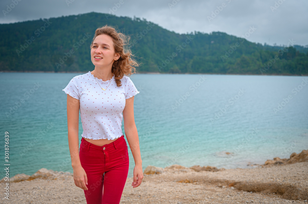 Young woman walking on the beach of a lake admiring the landscape and in the background wooded mountains in a cloudy sky