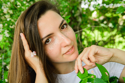 Young beautiful girl near the flowers. photon green and flowers. Portrait of young beautiful girl near flowers. Portrait of young beautiful woman, pretty face close-up, big pink lips, straight hair dr