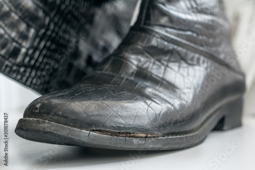 Old women's boots with side damage made of genuine leather imitating a crocodile pattern