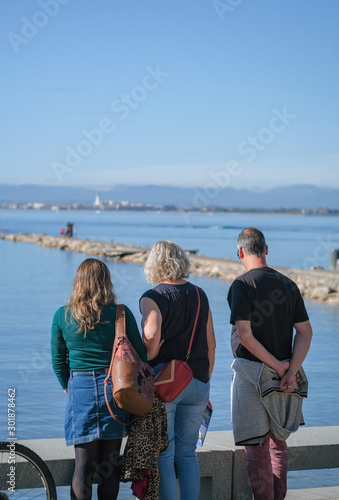 Elderly parents with an adult daughter look from the embankment, promenade to the calm sea in the bay. Autumn family vacation at sea, happy holidays. Hiking, walking along the sea in the sunny day.