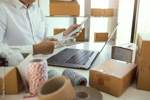 Asian man is holding a piece of paper to check the list of customer orders at his desk.