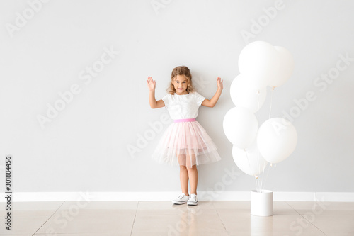 Little girl with balloons near light wall