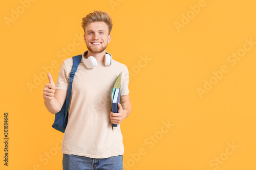 Portrait of male student showing thumb-up gesture on color background