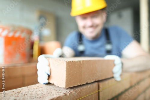 Fotografie, Obraz Male smiling builder puts make brickwork