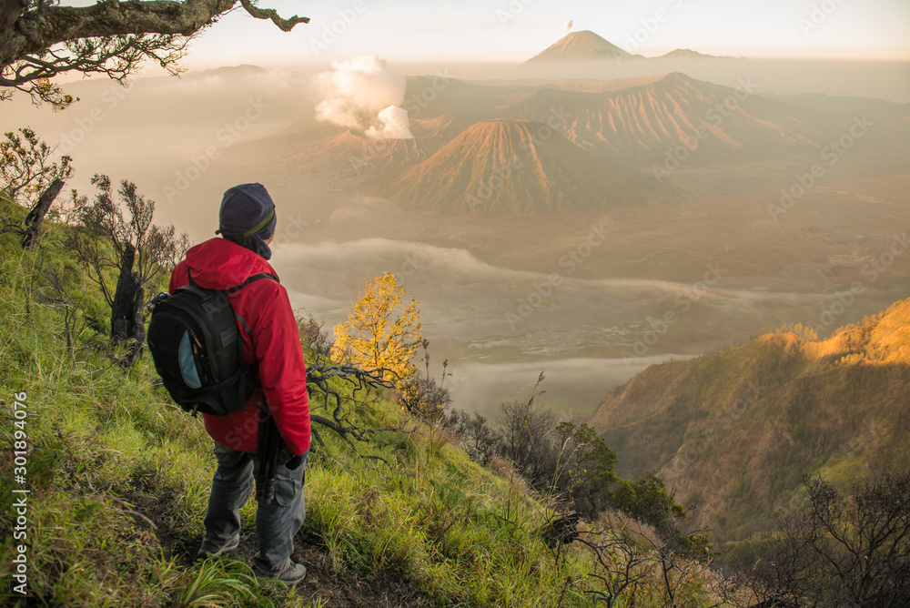 Back view of tourist standing on the hill and looking to the beautiful sunrise of Bromo Tengger Semeru National Park in East Java, Indonesia. 