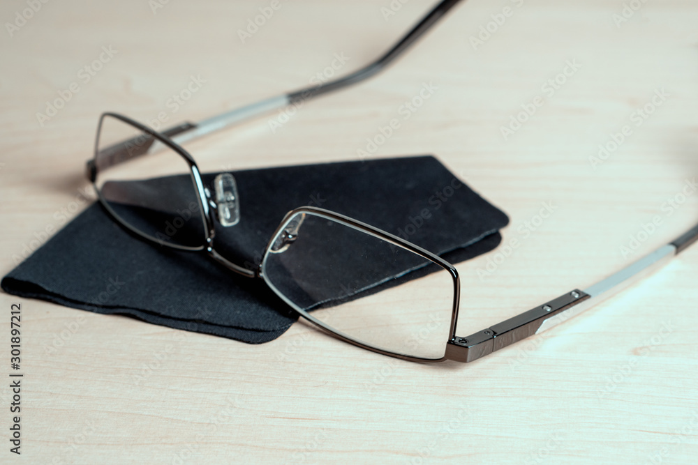 Glasses and cleaning cloth on a light wooden table. Eyeglass storage and care Glasses and cleaning cloth on a light wooden table. Eyeglass storage and care