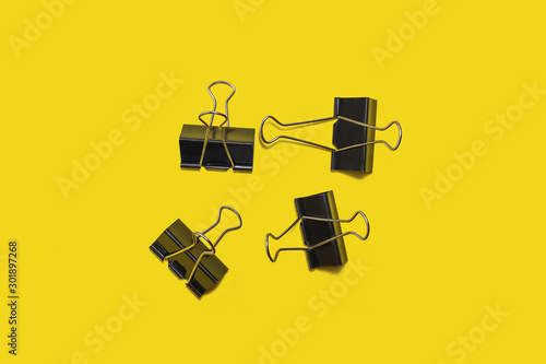 four black paper clip for office stationery lying isolated on yellow background. concept of business or educational equipment