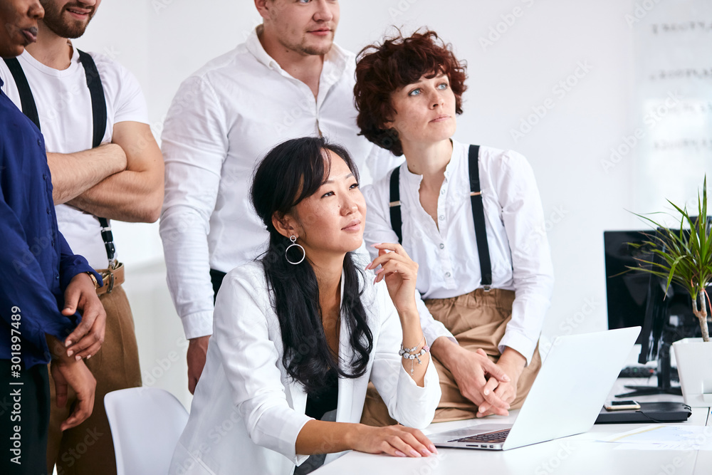 Obraz premium Attractive woman in white suit sitting with colleagues listen to coach in meeting room, white office interior
