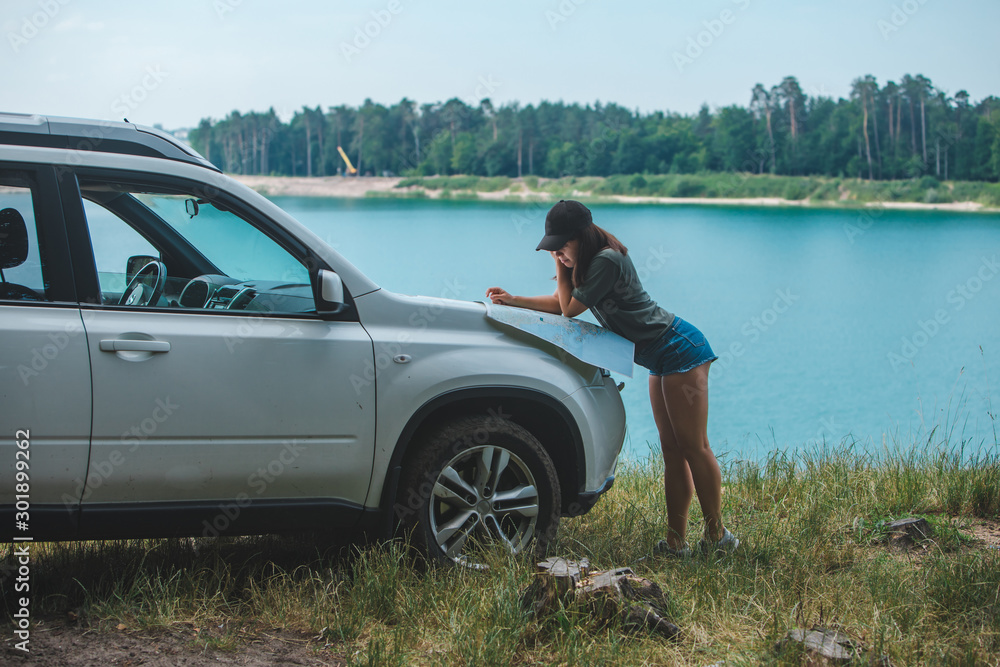 woman checking with map on the suv car hood lake with blue water on background