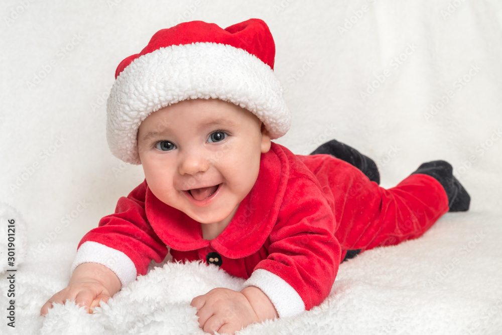 Little baby in Santa Claus costume is lying on white blanket Little baby in Santa Claus costume is lying on white blanket