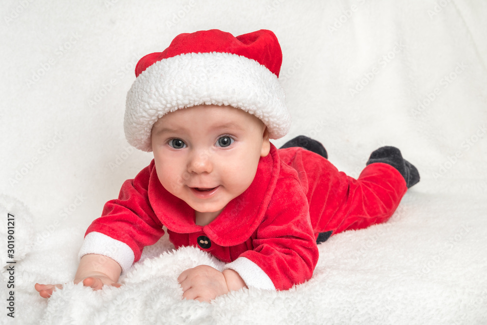Little baby in Santa Claus costume is lying on white blanket Little baby in Santa Claus costume is lying on white blanket