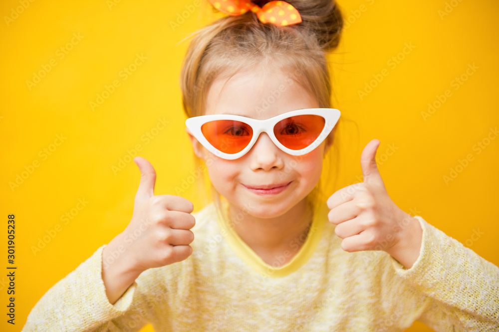 Portrait of child girl in sunglasses on yellow background, thumbs up Portrait of child girl in sunglasses on yellow background, thumbs up