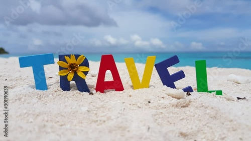 TRAVEL word with decor colorful letters and yellow tropical flowers on white sand in Pacific ocean background photo