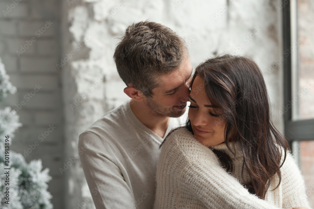 Loving couple on a light background celebrates Christmas kissing each other. Love, cares, warmth.