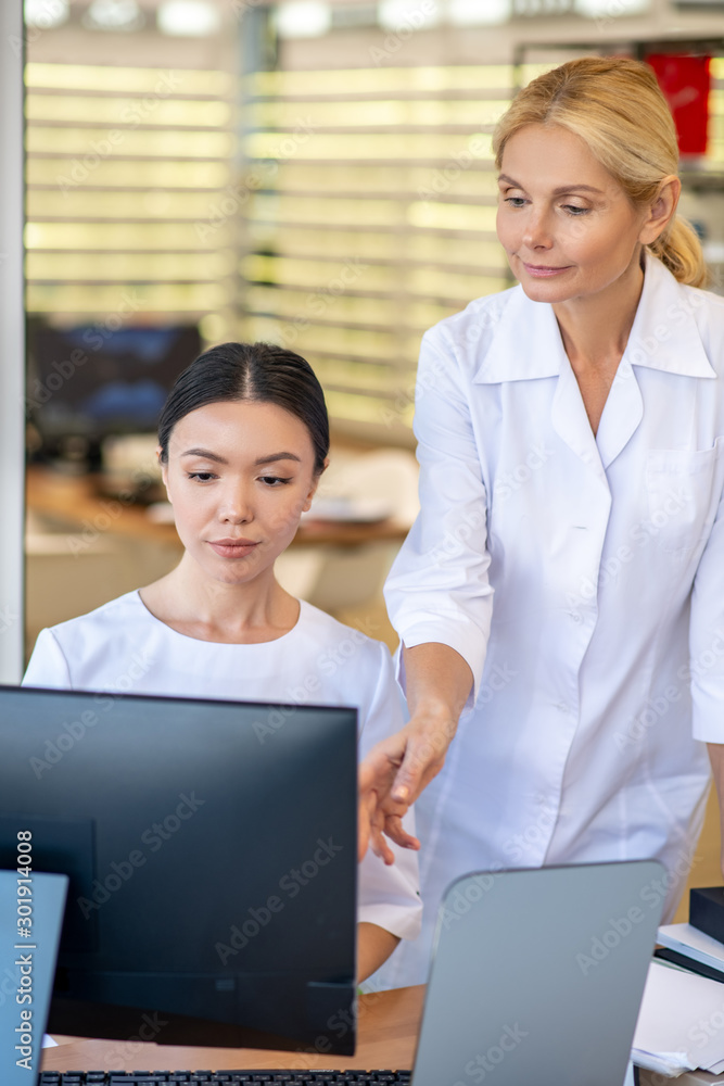 Dark-haired trainee of eye doctor sitting at the computer while learning process Dark-haired trainee of eye doctor sitting at the computer while learning process