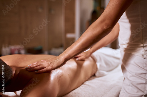 Gentle female hands with beautiful manicure of professional masseur, doing body relaxation massage to male client, health beauty resort wellness concept, shot from below