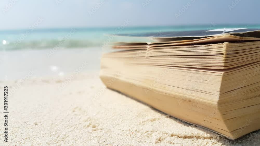 Static shot of a book sitting on the beach close up with waves crashing in the sand on the background in Seychelles 4K Static shot of a book sitting on the beach close up with waves crashing in the sand on the background in Seychelles 4K