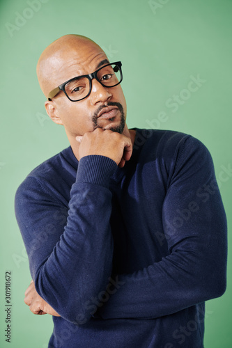 Portrait of intelligent muscular man in glasses thinking and looking at camera