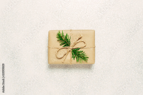 Craft Christmas gift decorated with a spruce twig on a shiny background, top view. DIY box.