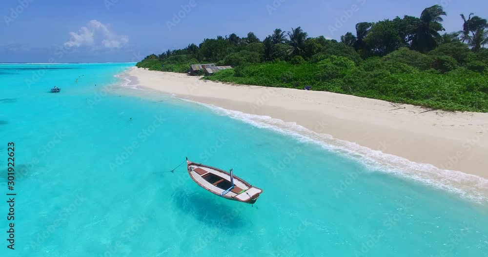 Drone static shot of a picturesque beach with a small wooden boat anchored on the shore, two wooden houses on the land and palm trees on the back 4K Bora Bora Drone static shot of a picturesque beach with a small wooden boat anchored on the shore, two wooden houses on the land and palm trees on the back 4K Bora Bora
