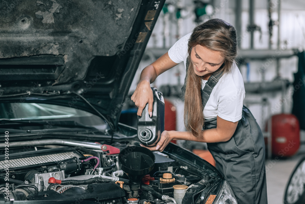 Beautiful Mechanic girl in a black jumpsuit and a white T-shirt changes the oil in a black car Beautiful Mechanic girl in a black jumpsuit and a white T-shirt changes the oil in a black car