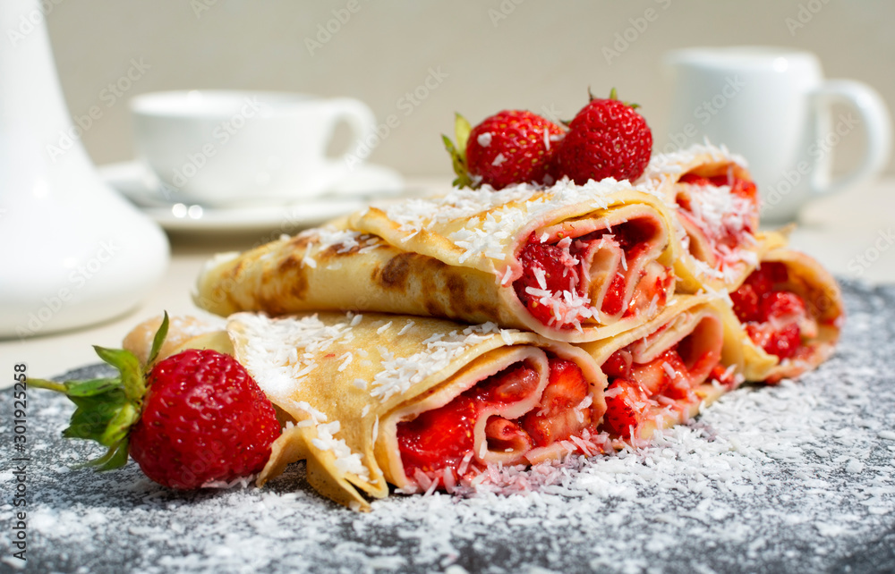 Rolled crepes or balkan pancakes stuffed fresh chopped strawberries, decorated powdered sugar and coconut flakes . Gourmet sweet dish Rolled crepes or balkan pancakes stuffed fresh chopped strawberries, decorated powdered sugar and coconut flakes . Gourmet sweet dish