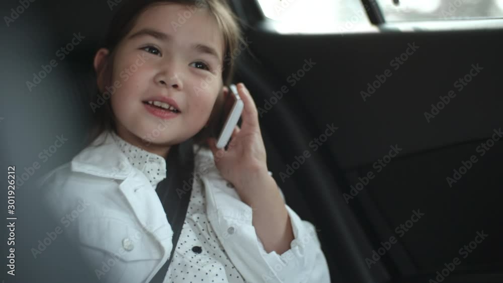 Cute little Asian girl riding in backseat in car and chatting on mobile phone Cute little Asian girl riding in backseat in car and chatting on mobile phone