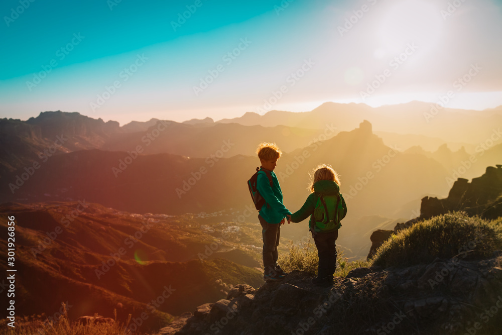boy and girl travel in mountains at sunset, kids holding hands, family hiking