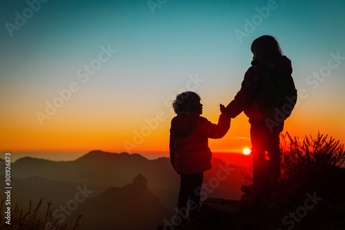 Silhouettes of happy kids hiking at sunset mountains