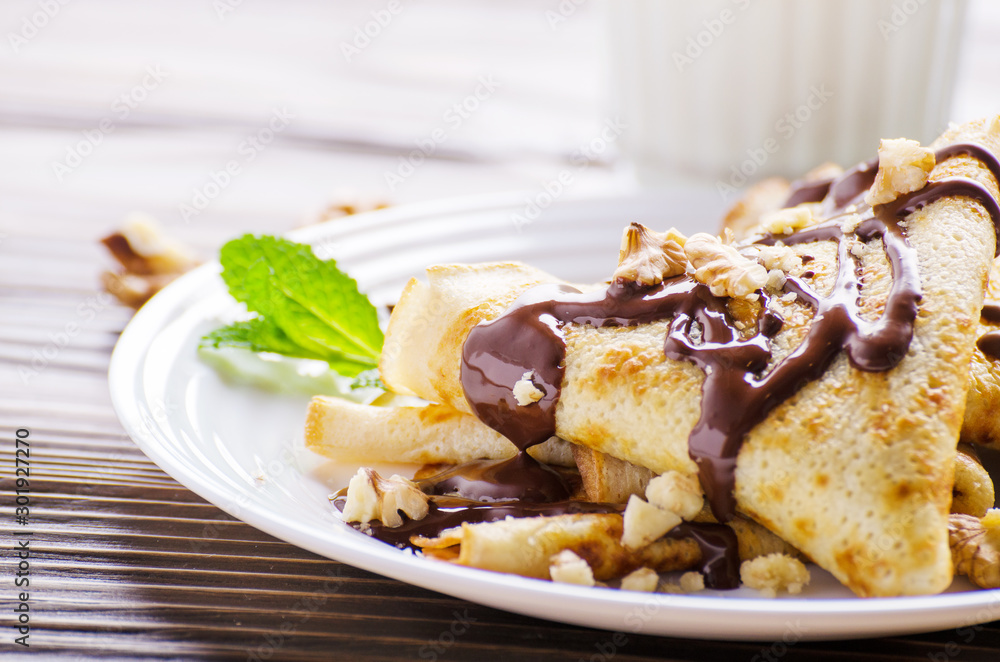 French crepes with chocolate sauce and walnuts in ceramic dish on wooden kitchen table French crepes with chocolate sauce and walnuts in ceramic dish on wooden kitchen table