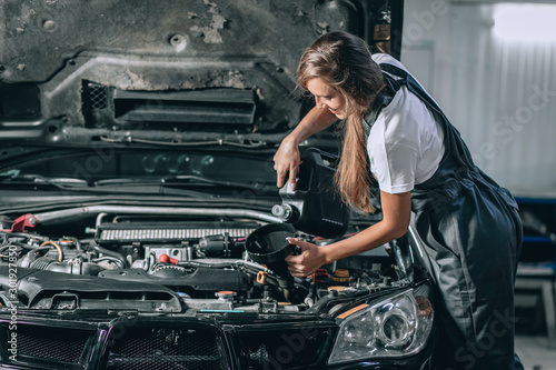 Beautiful Mechanic girl in a black jumpsuit and a white T-shirt changes the oil in a black car. car repair concept
