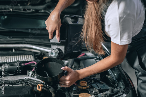 Beautiful Mechanic girl in a black jumpsuit and a white T-shirt changes the oil in a black car.close up photo. car repair concept