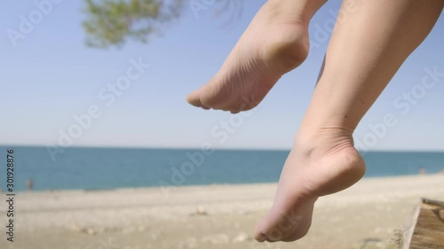 Female legs swing against backdrop of sea beach. Woman shakes legs on background of sea beach.