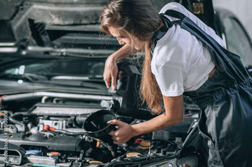 Beautiful Mechanic  girl in a black jumpsuit and a white T-shirt changes the oil in a black car. car repair concept © Semachkovsky 