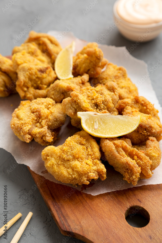 Homemade traditional japanese fried chicken Karaage on a rustic wooden board over gray surface, low angle view. Close-up. Homemade traditional japanese fried chicken Karaage on a rustic wooden board over gray surface, low angle view. Close-up.