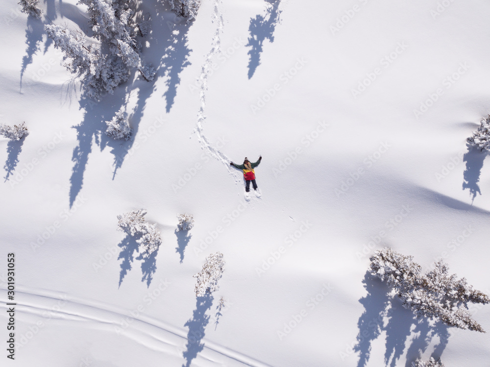 Winter aerial view portrait of Snowboarder female lying in clean snow between Christmas trees. Snowy mountain in ski resort, sunny winter holiday