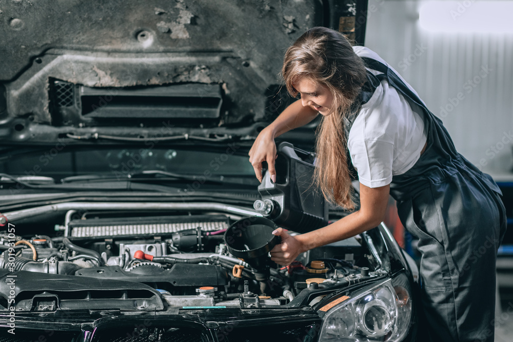 Beautiful Mechanic girl in a black jumpsuit and a white T-shirt changes the oil in a black car. car repair concept Beautiful Mechanic girl in a black jumpsuit and a white T-shirt changes the oil in a black car. car repair concept