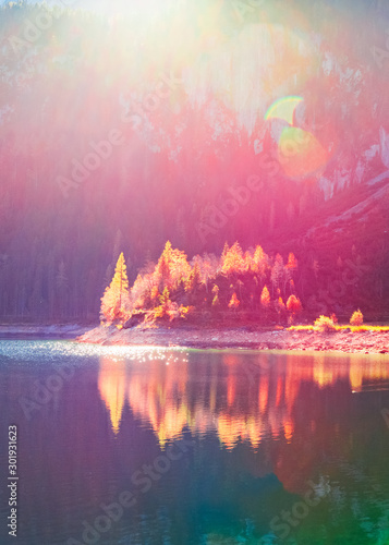 Amazing light during sunset on mountain lake in Dolomite Alps in Italy, South Tyrol area. Beautiful seasonal autumnal scene - small island in the middle of lake with colorful yellow trees.