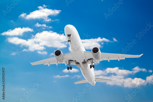 white passenger plane has released its landing gear and is coming in to land with background of white clouds and blue sky