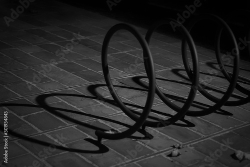 Monochromatic shot of shadows and lights created by a street lamp, which illuminates at night a spiral for bicycle support