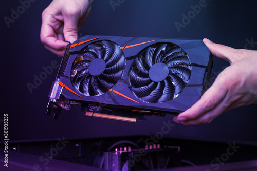 Mounting a modern graphic card to gaming computer. High performance graphics card with two coolers. The hands place the card in the computer case.