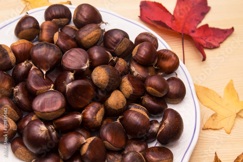plate of chestnuts on wooden background and leaves