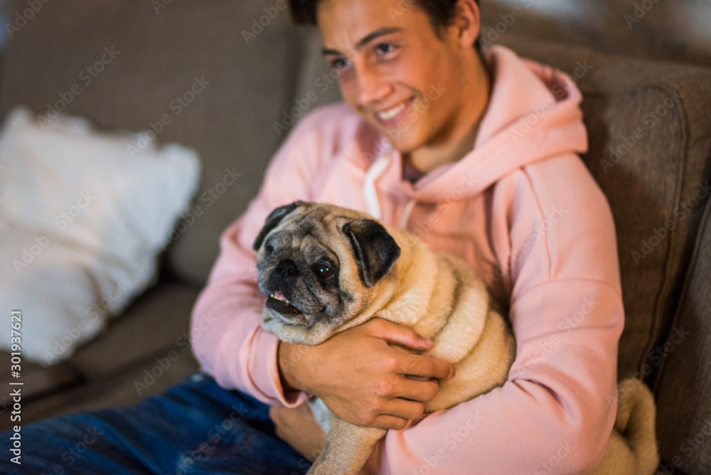 Fototapeta pug and teenager together hugged on the sofa - pet and domestic dog at home