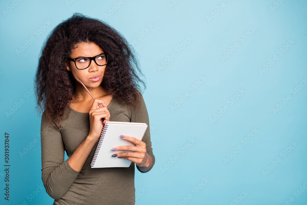 Portrait of pensive minded dark skin girl in spectacles clever smart intelligent hipster think thoughts to write essay hold copybook pen wear stylish outfit isolated over blue color background - obrazy, fototapety, plakaty 