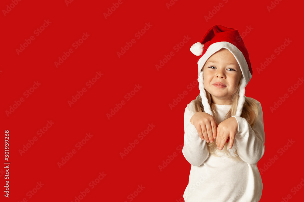 Portrait of little pretty girl in Santa hat isolated on red background. Happy Christmas holidays, cute child in happiness. Portrait of little pretty girl in Santa hat isolated on red background. Happy Christmas holidays, cute child in happiness.