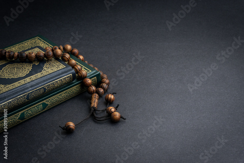 Holy Quran with arabic calligraphy meaning of Al Quran and tasbih or rosary beads on black background. Selective focus and crop fragment photo