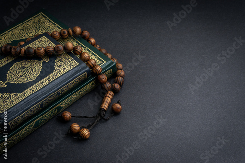 Holy Quran with arabic calligraphy meaning of Al Quran and tasbih or rosary beads on black background. Selective focus and crop fragment