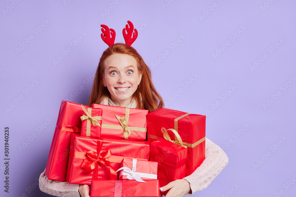 Close view of charming young model with with happy smiling face, holding red boxes with Christmas presents, expressing joyfulness, spending pleasant time by receiving beautiful gifts Close view of charming young model with with happy smiling face, holding red boxes with Christmas presents, expressing joyfulness, spending pleasant time by receiving beautiful gifts