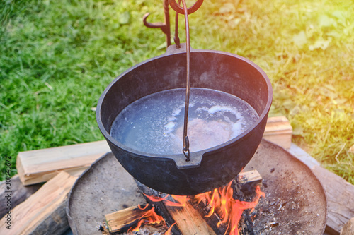 Pot with a piece of meat in the broth hung on the fire. Boiler with soup on a summer day, lifestyle.