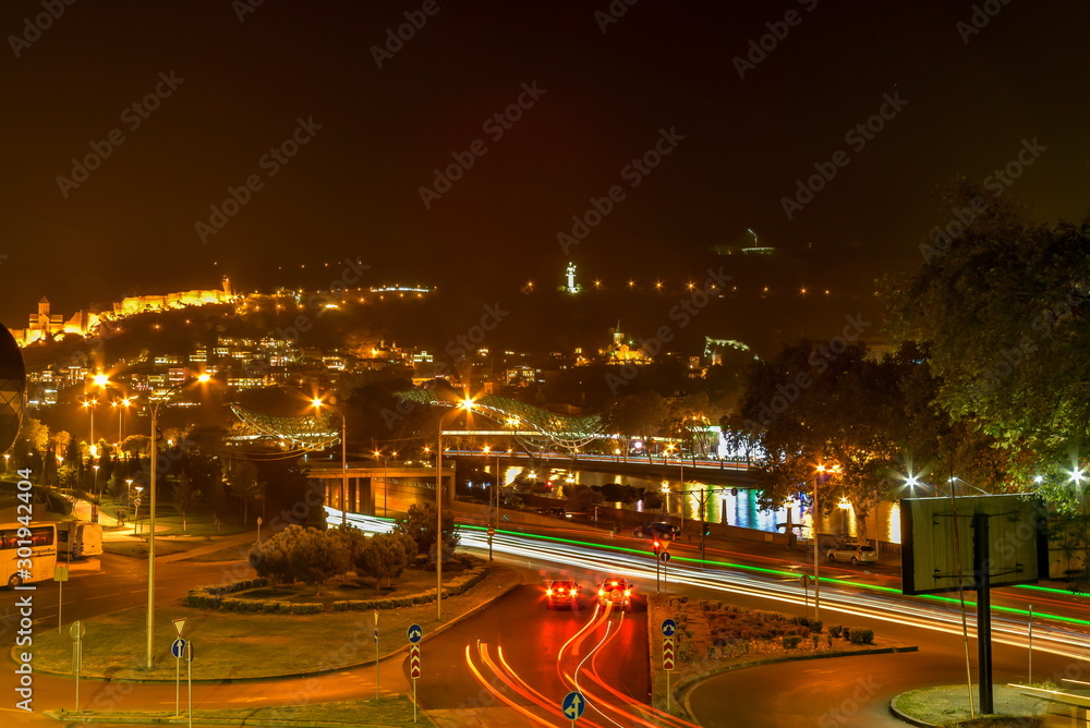 Fototapeta premium Pedestrian Bridge of Peace over the Kura River, Narikala Fortress and Kartlis Deda Monument in Tbilisi, Georgia